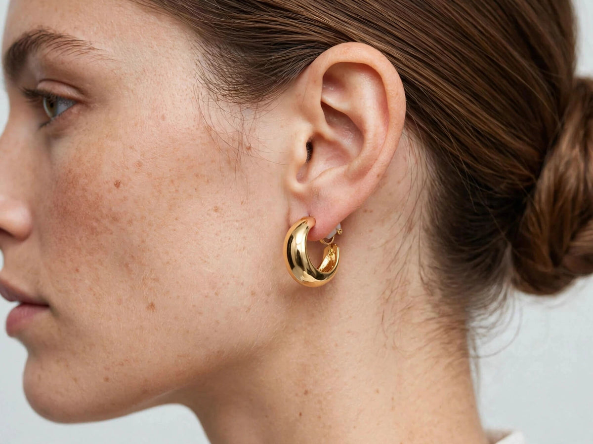 Model wearing polished gold-tone C-shape clip-on earrings with a rounded hoop silhouette