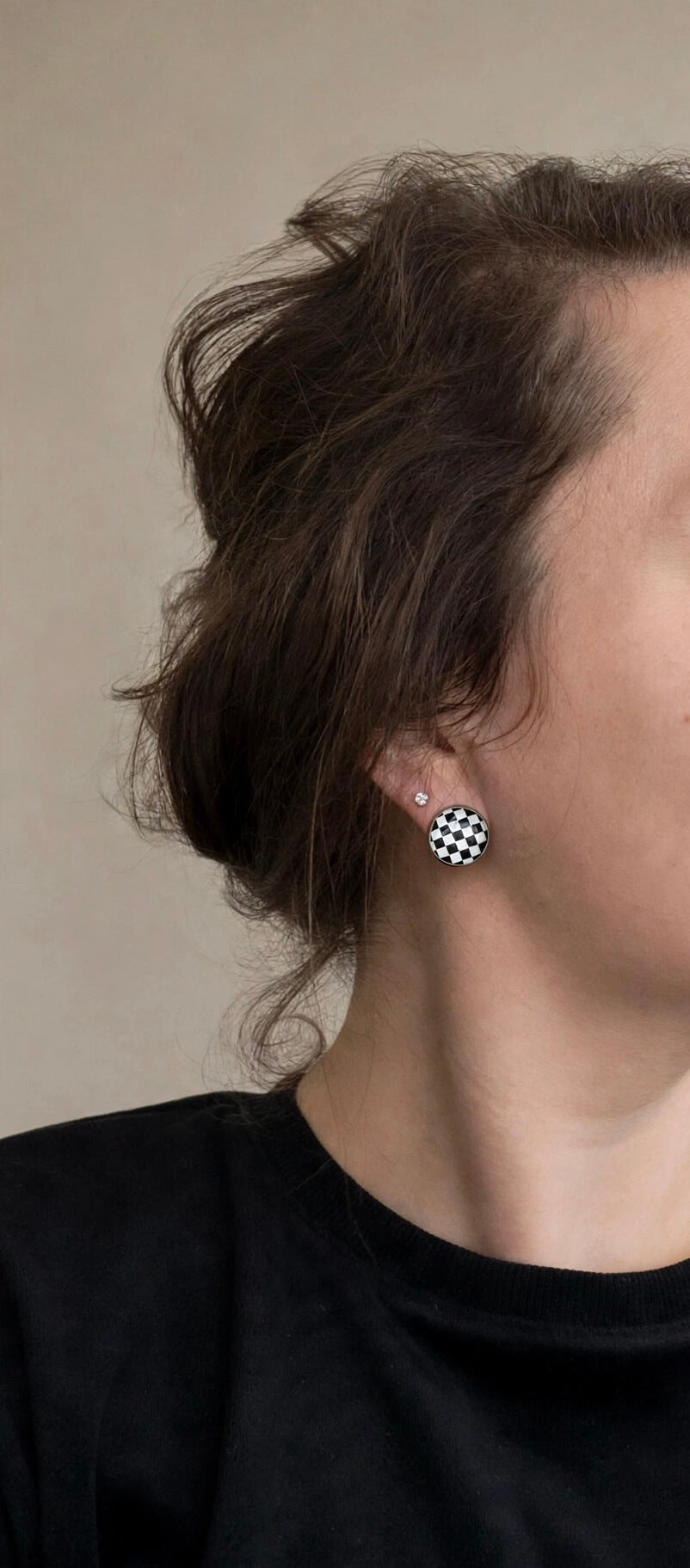 Model wearing a round black and white checkerboard clip-on earring