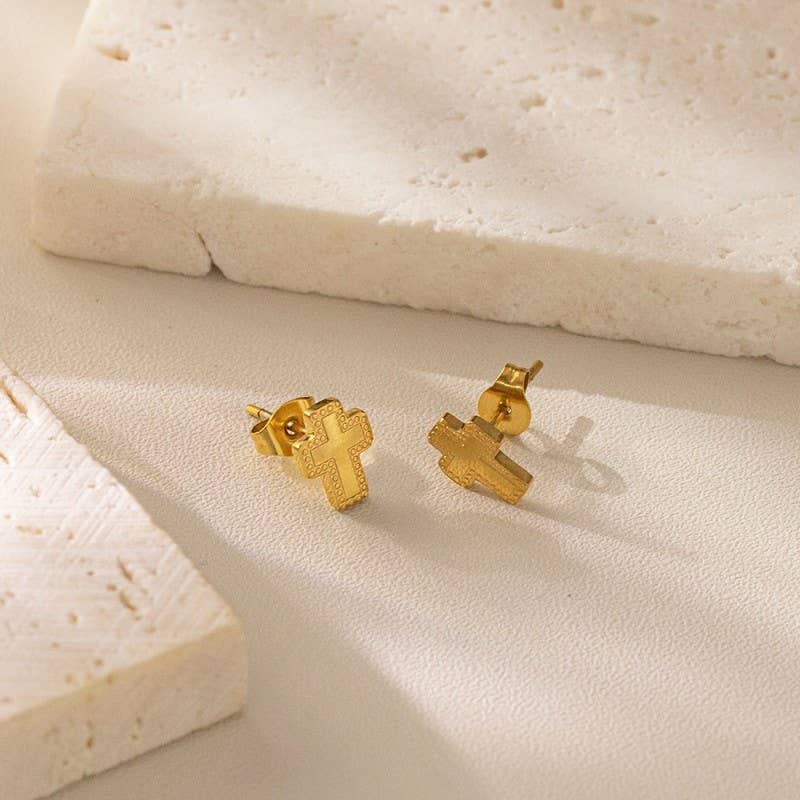 Gold cross earrings on a textured beige surface