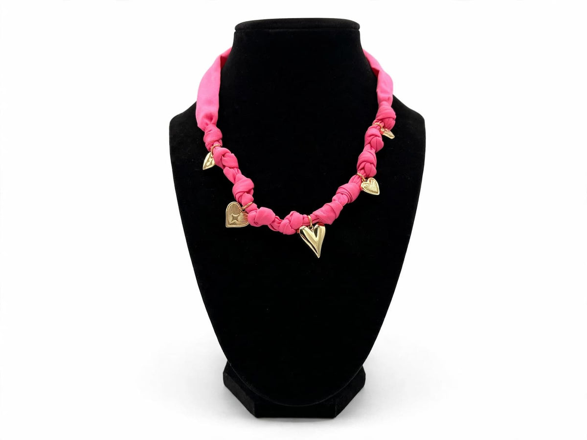 Bright pink fabric necklace with gold-colored heart charms displayed on a black jewelry bust.