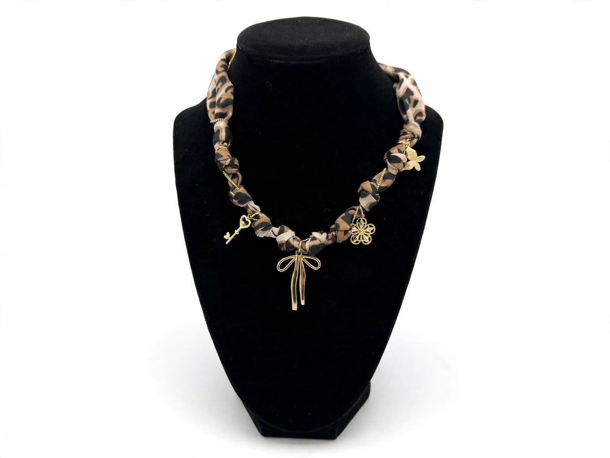 Leopard-print fabric necklace with gold-colored charms displayed on a black jewelry bust.