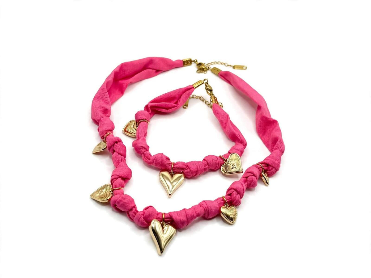 Bright pink fabric necklace and matching bracelet with gold-colored heart charms on a white background.