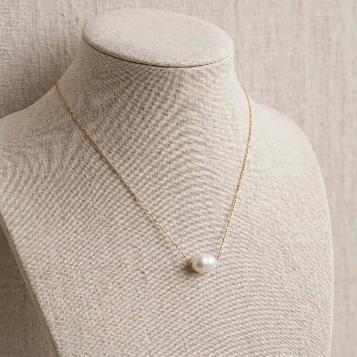 Single white freshwater pearl pendant necklace on a beige jewelry bust.