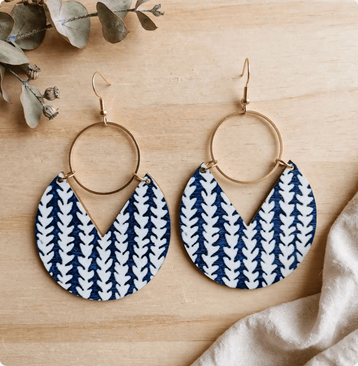 Blue-and-white patterned wooden drop earrings with gold-tone rings on a wooden background