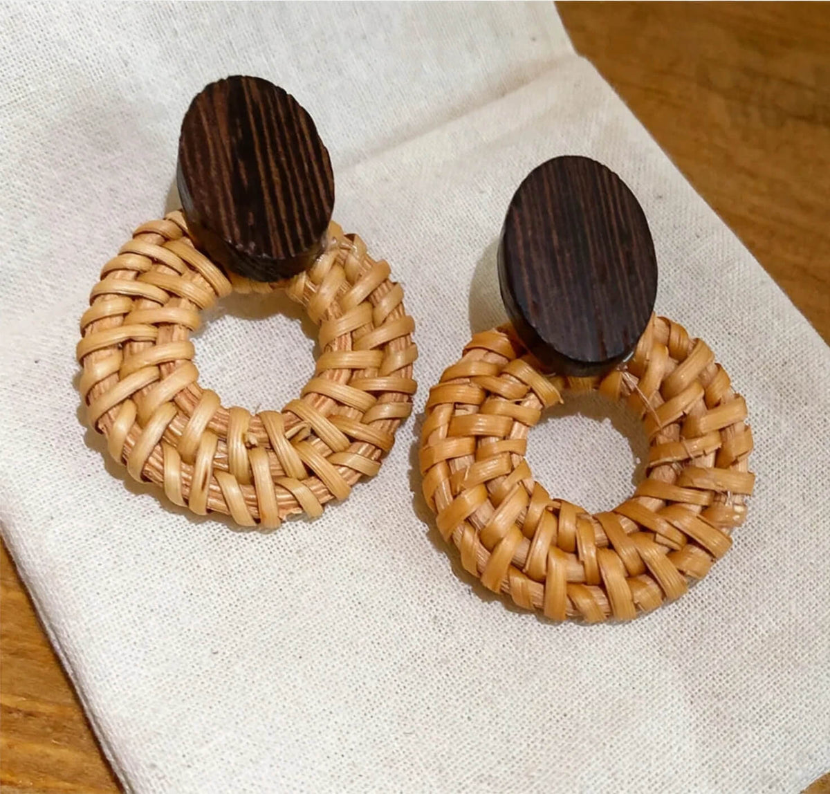 Tan handwoven straw statement earrings with dark brown wood oval tops.
