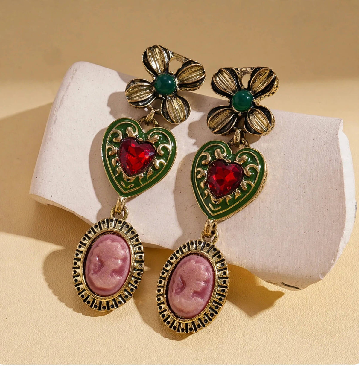 Vintage-inspired dangle earrings with pink cameo-style portraits, red heart rhinestones, and green floral accents.