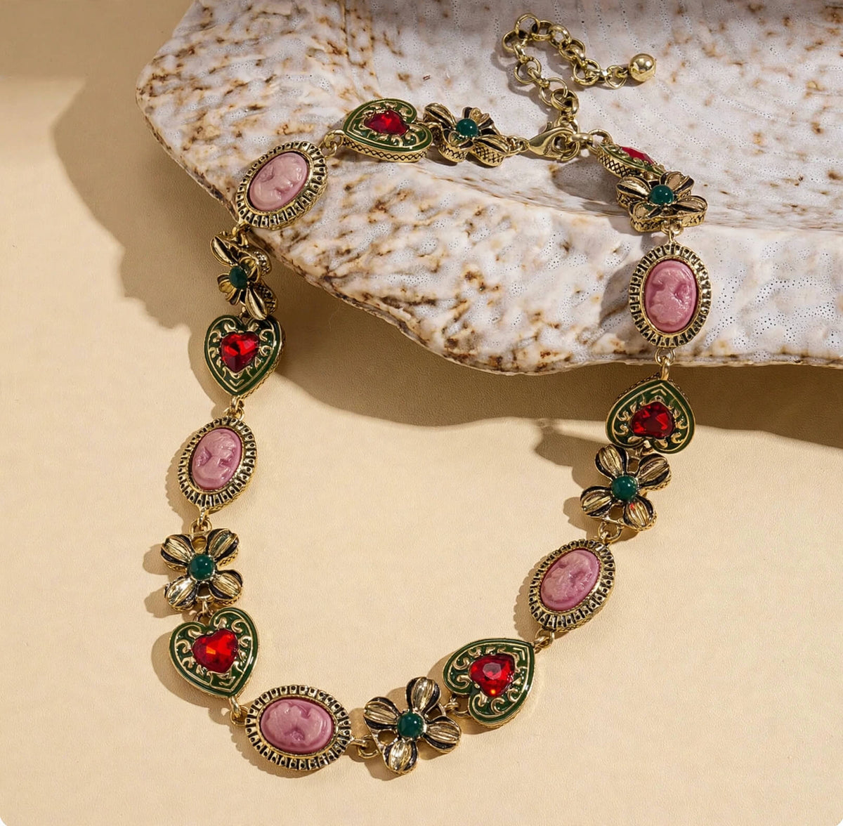 Vintage-inspired necklace with pink cameo-style portraits, red heart rhinestones, and green floral accents.