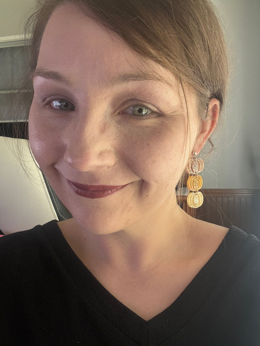 Layered glitter pumpkin dangle earrings in brown, golden amber, and clear tones on a black jewelry stand