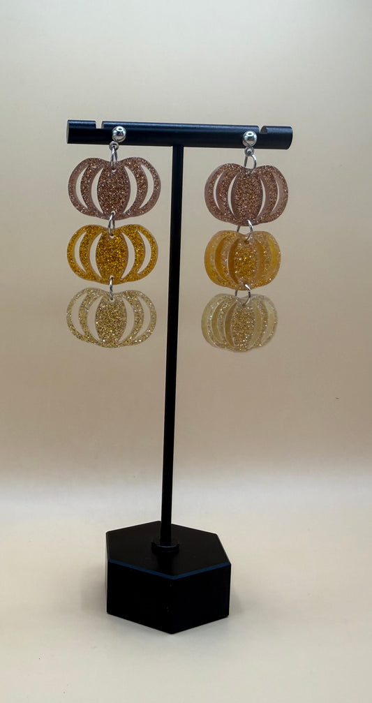Model wearing layered glitter pumpkin dangle earrings in warm autumn colors